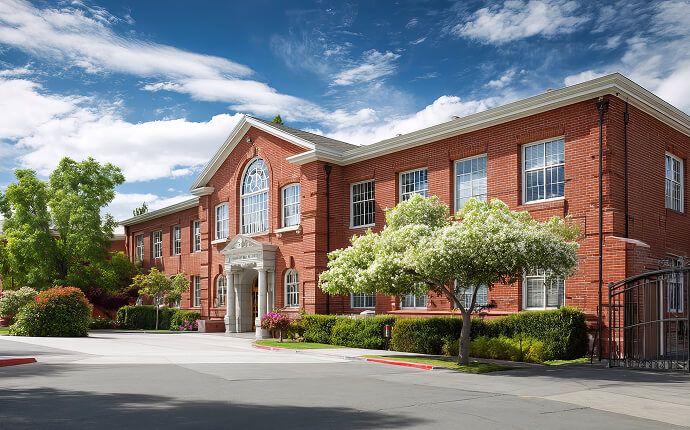 The front of a large educational institute under a sunny, blue sky and surrounded by trees and greenery